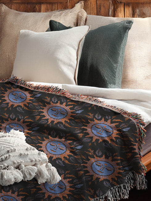 Luxurious woven cotton throw blanket featuring mystical blue sun faces with copper rays on black background, bordered by elegant fringe. Perfect celestial wall hanging, witchy bedroom decor, or dark academia throw for couch or bed.